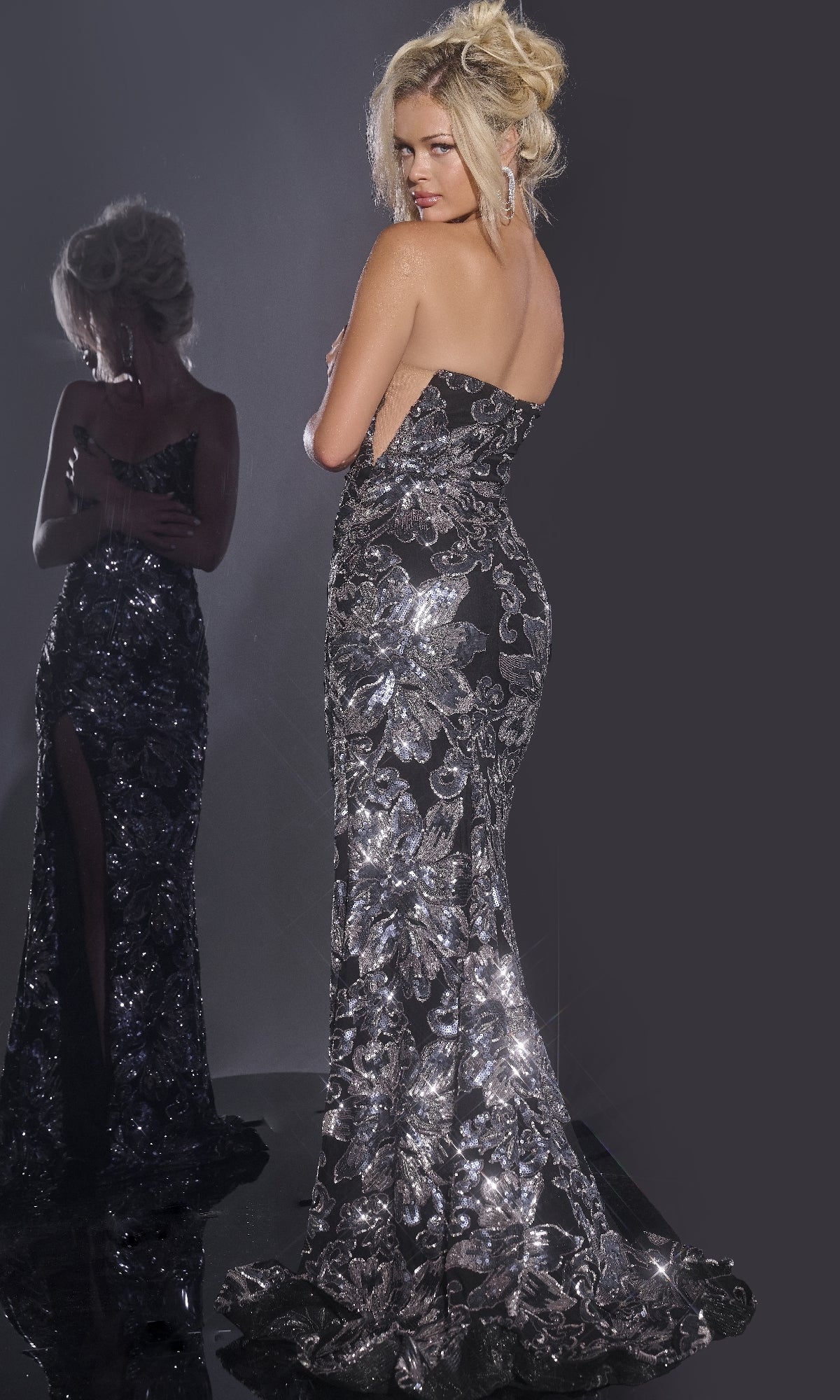 A woman in the Jovani 44116 Strapless Floral-Sequin Prom Gown stands with her back turned, reflected in a mirror against a dark background.